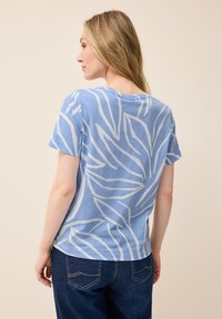 Ljusblå t-shirt med kort ärm som har vita bladmönster. Tillverkad av mjukt tyg med en avslappnad passform och rund halsringning.