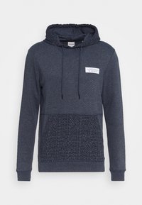 Felpa blu navy con coulisse, tasca frontale a soffietto con testo ripetuto "Jack & Jones", e una toppa bianca etichettata "CORE" sul petto.