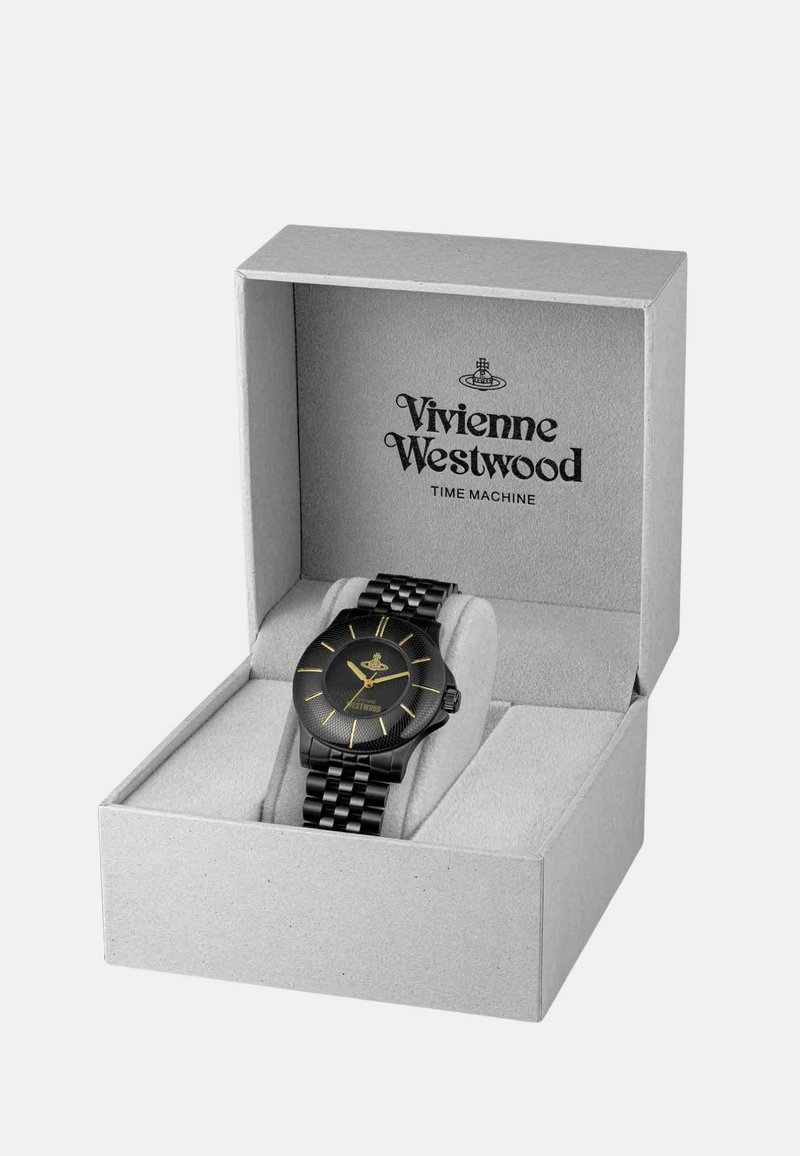 Montre noire avec un cadran rond texturé, des accents dorés et un bracelet en métal noir, présentée dans une boîte grise avec le nom de la marque imprimé à l'intérieur.