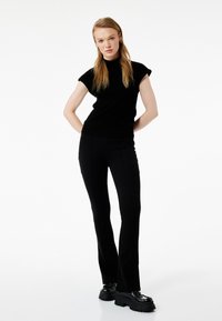 Top negro ajustado con cuello alto y mangas cortas, combinado con pantalones acampanados negros de talle alto. La modelo lleva unos zapatos de plataforma chunky negros.