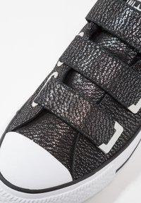 Czarny sneaker z materiałem odblaskowym, wyposażony w trzy paski na rzep, biały gumowy nosek i teksturowane zdobienia na cholewce.