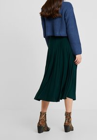 Avklippt blå kabelstickad tröja, veckad mörkgrön midikjol och klackboots i snakeskin-mönster. Texturerade material är synliga.