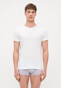 Weißes Baumwoll-T-Shirt mit Rundhalsausschnitt und kurzen Ärmeln, kombiniert mit hellgrauen Boxershorts. Einfaches Design mit minimalem Branding.
