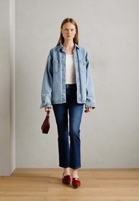 Heledsinine ülev suur denim jope valge pluusi peal, tumedatest sinistest flare-stiilis teksadest ja punastest loafidest koos. Hoides väikest punast käekotti.