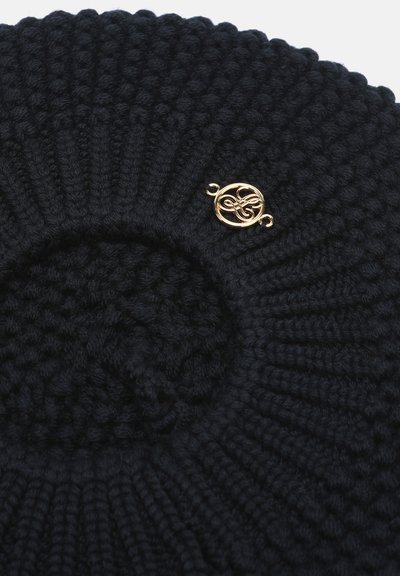 Béret rond noir en maille avec des côtes texturées et une petite broche décorative dorée brillante fixée près du bord.