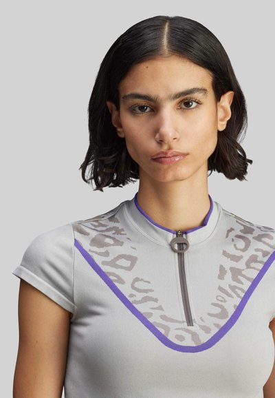 Hihaton harmaa paita, jossa korkea kaulus, violetti korostus ja puolivetoketju. Edessä on hienovarainen eläinkuosi.