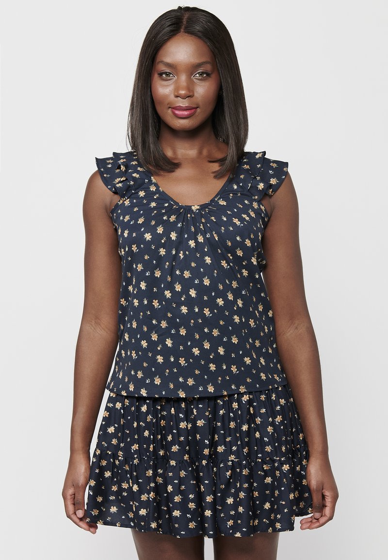 Abito floreale navy con gonna a strati e volant. Presenta maniche corte con volant e scollatura arricciata, decorata con piccoli fiori gialli e bianchi.