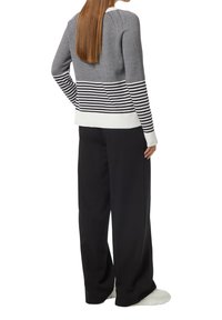 Grauer gestrickter Pullover mit horizontalen schwarzen und weißen Streifen am Saum, kombiniert mit lockeren schwarzen Hosen und weißen Schuhen.