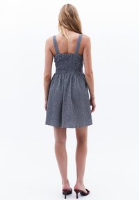 Mekko, jossa on musta-valkoinen ruudullinen kuosi, smockattu yläosa, ohuet hihat ja liehuva helma, valmistettu kevyestä kankaasta.