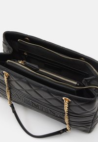 Sac à main en cuir matelassé noir avec des accents en chaîne dorée, plusieurs poches intérieures et un compartiment zippé. Présente une marque en relief.
