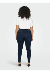 Hög midja, mörkblå skinny jeans i denim-material, med bakfickor med en subtil design, kombinerat med en vit T-shirt och svarta klackar.