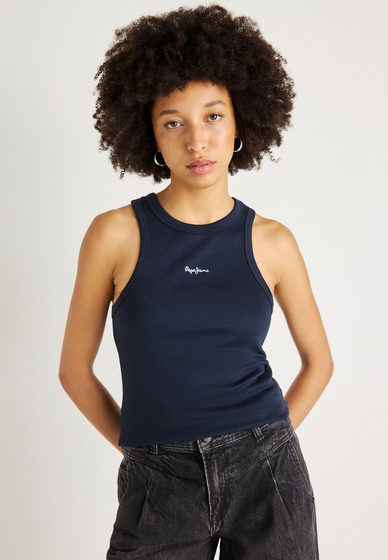 Marineblå ribbestrikket tanktop med rund hals, med en liten hvit logo i midten. Kombinert med høy midje svarte jeans.