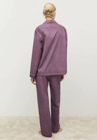 Lila denimjacka och matchande byxor med en avslappnad passform, synlig sömnad och en mjuk textur. Utsikt från baksidan.
