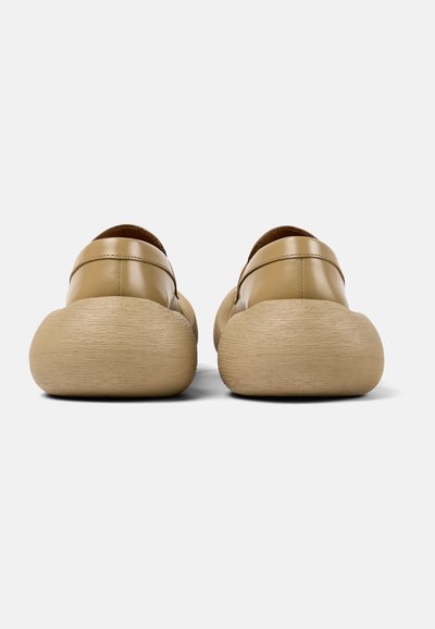 Zapatos de cuero beige con un acabado suave y suelas redondeadas con textura de madera. Diseño minimalista sin herrajes ni acentos prominentes.