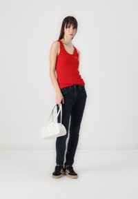 Un débardeur rouge à côtes avec un décolleté arrondi, associé à un jean skinny foncé et des baskets noires ; tenant un sac à main blanc. Design simple.