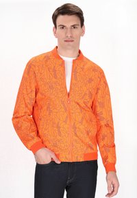 Giacca bomber arancione brillante con un motivo geometrico in un arancione più chiaro. Presenta una chiusura a zip e polsini e cintura a costine.