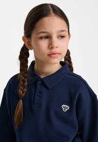 Marinblå polo skjorta med en texturerad tyg, med krage, två knappar och en liten broderad logotyp på vänster bröst.