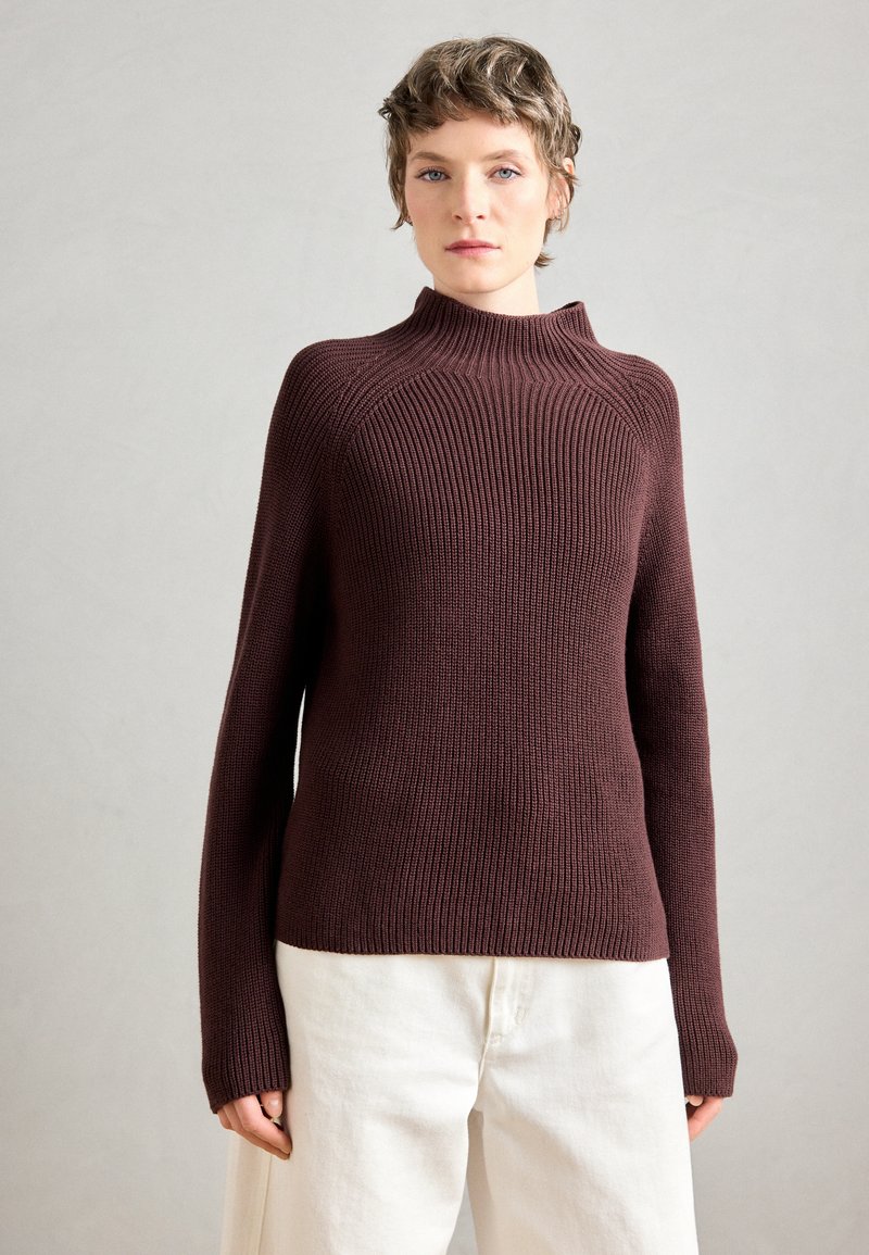 Maglione a coste bordeaux con collo alto, maniche lunghe e silhouette aderente, abbinato a pantaloni bianchi a gamba larga.