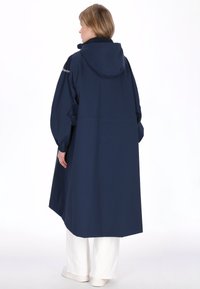 Tengerészkék vízálló kabát kapucnival, hosszú ujjal és egyenes szabással. Hátsó varrással, rugalmas mandzsettával és laza fazonnal rendelkezik.