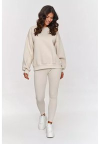 Beżowy, oversize'owy sweter z obniżonymi ramionami, zestawiony z prążkowanymi legginsami w pasującym kolorze. Białe sneakersy dopełniają look.