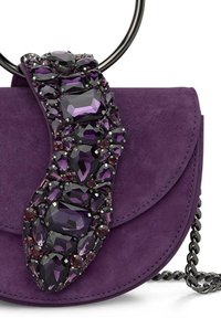 Fioletowa torebka z zamszu z wyraźnym paskiem ozdobionym biżuterią, na którym znajdują się różnorodne kształty kamieni szlachetnych. Łańcuszkowy pasek na ramię jest wykonany z czarnego metalu.