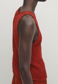 Débardeur tricoté rouge avec un design sans manches, des côtés ouverts et une texture côtelée, présentant des coutures lâches et définies.