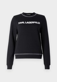 Melnā džemperis ar garām piedurknēm. Uz krūšu daļas ir balts teksts "KARL LAGERFELD" un balta apmale apakšmalā. Mīkstais kokvilnas audums.