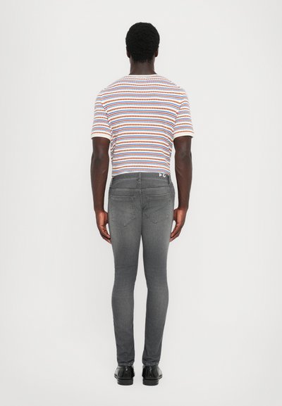 Ταιριαστό ανδρικό μπλουζάκι με ρίγες σε λευκό, κόκκινο, μπλε και πορτοκαλί, συνδυασμένο με σκούρα γκρι στενά τζιν. Η μπλούζα διαθέτει κοντά μανίκια.