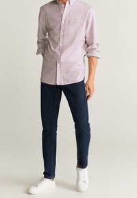 Rode en witte gestreepte overhemd met knopen, smalle navy jeans en witte sneakers. Het overhemd heeft een borstzak en opgerolde mouwen.