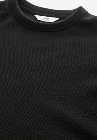 Pull en coton noir avec un design en tricot gaufré texturé et un col rond, comportant une étiquette indiquant "NEXT RELAXED FIT" à l'intérieur.