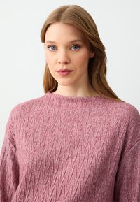 Maglione a collo rotondo con texture in rosa chiaro, caratterizzato da un motivo a rombi e maniche lunghe. Il tessuto appare morbido e lavorato a maglia.