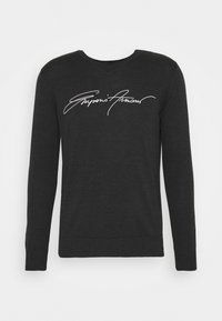Black long-sleeve sweater with a V-neck and a fitted hem. Features a white signature logo across the chest. Made of a smooth, stretchy fabric.