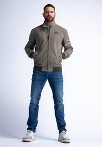 Khaki bomberová bunda s stojatým límcem, zapínáním na zip a dvěma předními kapsami. Nosit s modrými džíny a světlými teniskami.