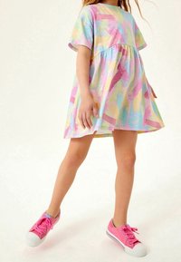 Värikäs lyhythihainen mekko, jossa on kerroksellinen muotoilu vaaleanpunaisen, sinisen ja keltaisen pastelliväreissä. Yhdistetty kirkkaan vaaleanpunaisiin lenkkareihin.