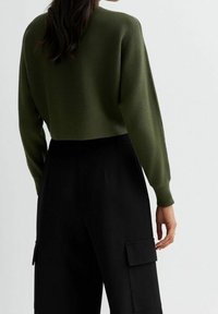 Oliivinvihreä, ribbikuvioitu lyhyt neulepusero pitkillä hihoilla, yhdistetty mustiin, korkeavyötäröisiin cargo-housuihin, joissa on sivutaskut.