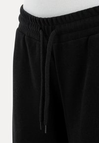 Zwarte joggingbroek met tailleband van elastiek en lange trekkoorden, getoond op een wit mannequintorso.