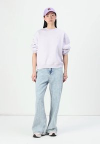 Sweatshirt oversized de culoare violet deschis, cu manșete cu nervuri, asortat cu blugi largi de culoare bleu deschis și o șapcă de baseball lila. Tenisii completează ținuta.