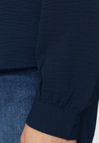 Dunkelblaues, strukturiertes Hemd mit langen Ärmeln und gerafften Manschetten, kombiniert mit Denim-Stoff in einer ausgebleichten Waschung.