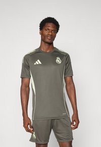 Jersey atlético gris con detalles en verde claro, que presenta el logo del Real Madrid. Diseño de manga corta y cuello redondo, hecho de una tela ligera.