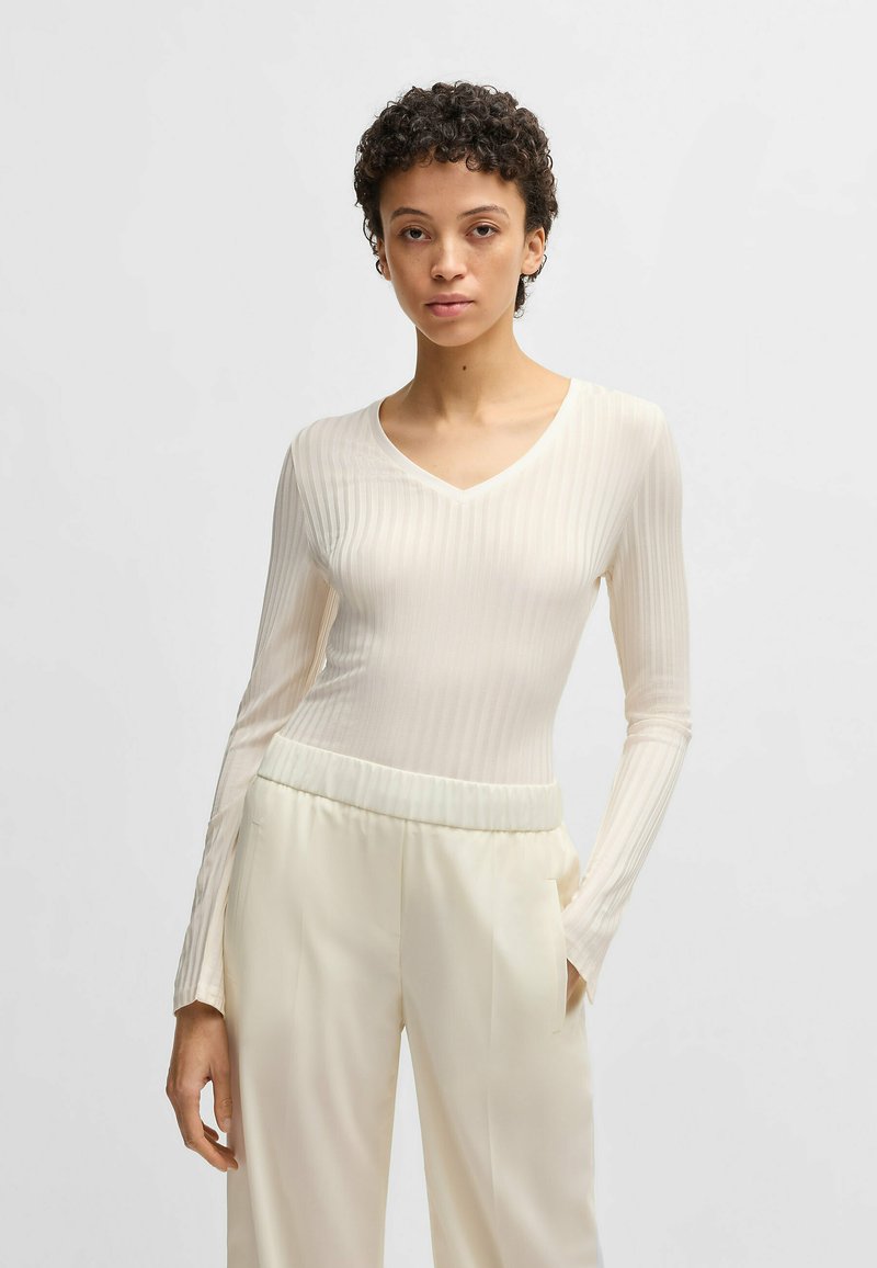 Long-sleeve, cream v-neck top with vertical ribbing texture, paired with wide-legged light beige trousers featuring an elastic waistband.