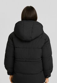 Svart puffjacka med huva, med en quiltad design, medellång passform och elastiska ärmslut. Slät textur, ingen synlig hårdvara.