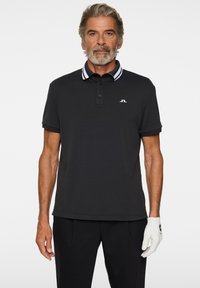 Musta poolopaita klassisella designilla, jossa valkoiset raidalliset kauluksen yksityiskohdat ja pieni logo rinnassa. Pestävä kangas, rento istuvuus.