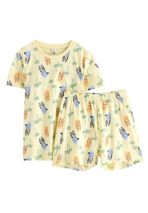 Gult sæt med kortærmet skjorte og shorts med farverige tegneseriehundes ansigter og grønne palmebladsmønstre.