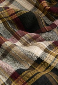 Tissu tissé avec un motif à carreaux dans des teintes de bordeaux, noir, jaune et beige. Surface texturée avec des plis doux et irréguliers et une épaisseur de fil variable.