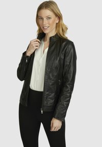 Black leather jacket featuring a stand-up collar, front zipper closure, and two side zippered pockets, paired with a white blouse and black leggings.