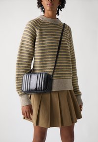 Borsa a tracolla nera trapuntata con accessori in argento; presenta una forma rettangolare e una finitura testurizzata. Indossata sopra un maglione a righe.