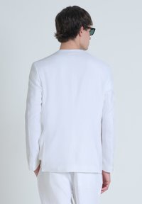 Blazer de lino blanco visto desde la parte de atrás, con un corte recto, mangas largas y costuras sutiles a lo largo del dobladillo.