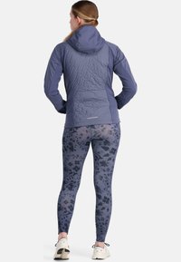 Veste à capuche navy avec un dos texturé et leggings à motif floral, portés avec des chaussures de course de couleur claire.