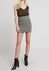 Oliivinvihreä satiininen toppi napilla, yhdistettynä ruutukuosisella minihelmalla. Mustat patenttipintaiset nilkkurit, joissa on paksut korot.