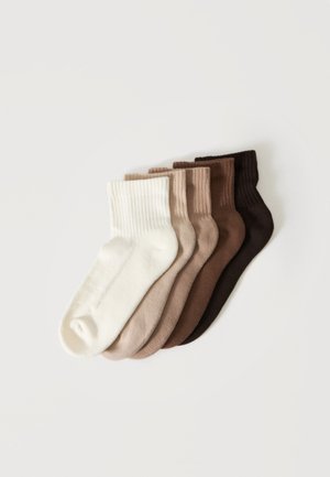 Five pairs of ribbed ankle socks arranged in a fan, colors ranging from white to dark brown on a plain background.